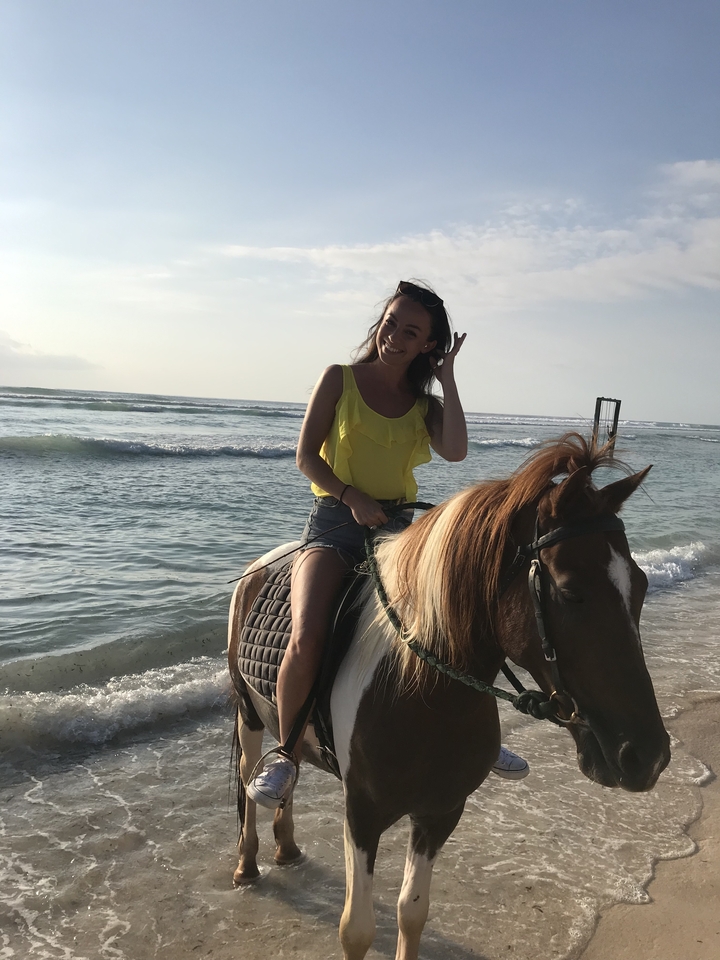 Woman riding a horse on a beach with waves in the background.