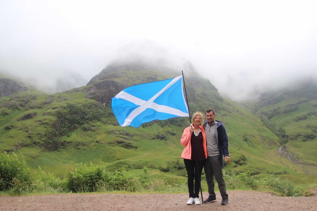 Couple posing with a Scottish flag in a foggy mountainous landscape.