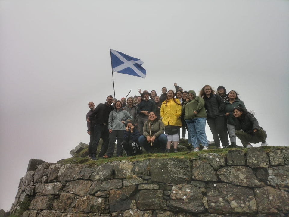 Group of people celebrating with a Scottish flag on a hilltop.