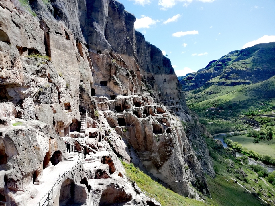 Dramatic cliffside cave dwellings and terraces of Vardzia Monastery overlooking a green river valley and distant peaks.