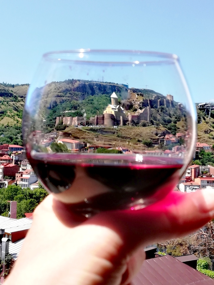Creative shot of a glass of red wine in focus with Tbilisi’s Narikala Fortress and old town blurred inside the glass.