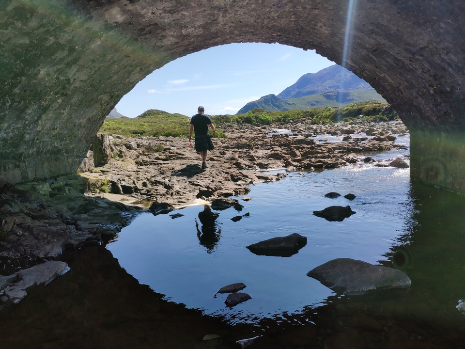 Person walking under a stone bridge over a rocky stream.