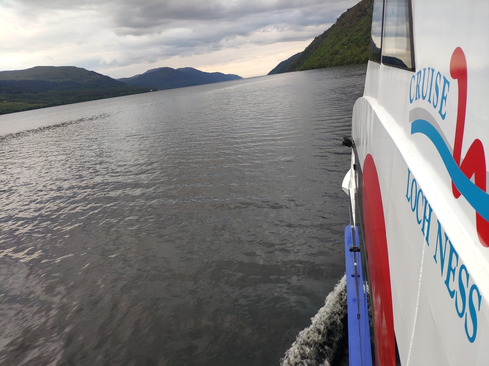 Boat on a lake with scenic hills in the background labeled 'Loch Ness'.