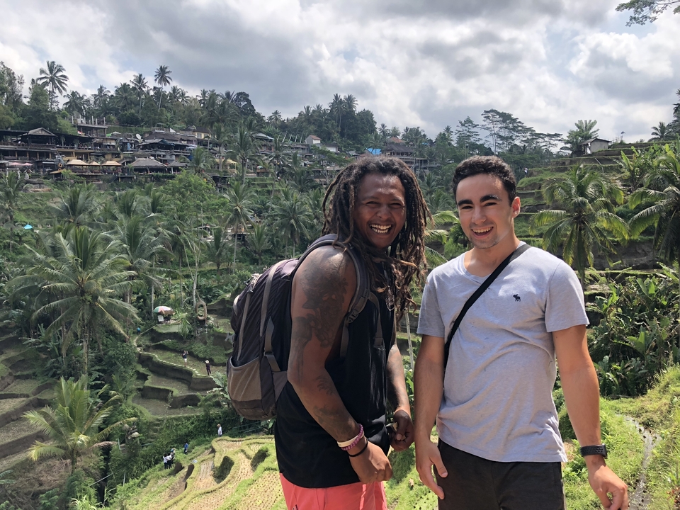 Two men smiling with a backdrop of terraced rice fields.