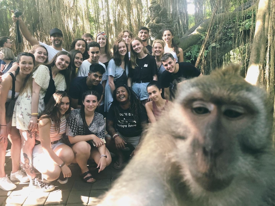 Large group of people with a monkey selfie in a tropical area.