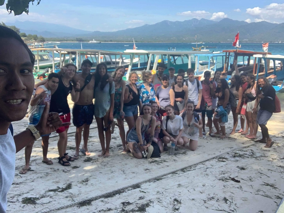 Group of people posing on the beach with boats in the background.