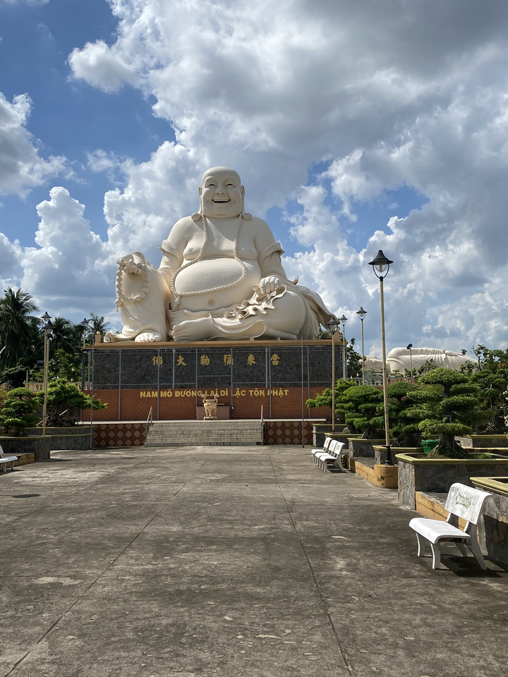 A large Buddha statue sitting on a decorated platform in a park.