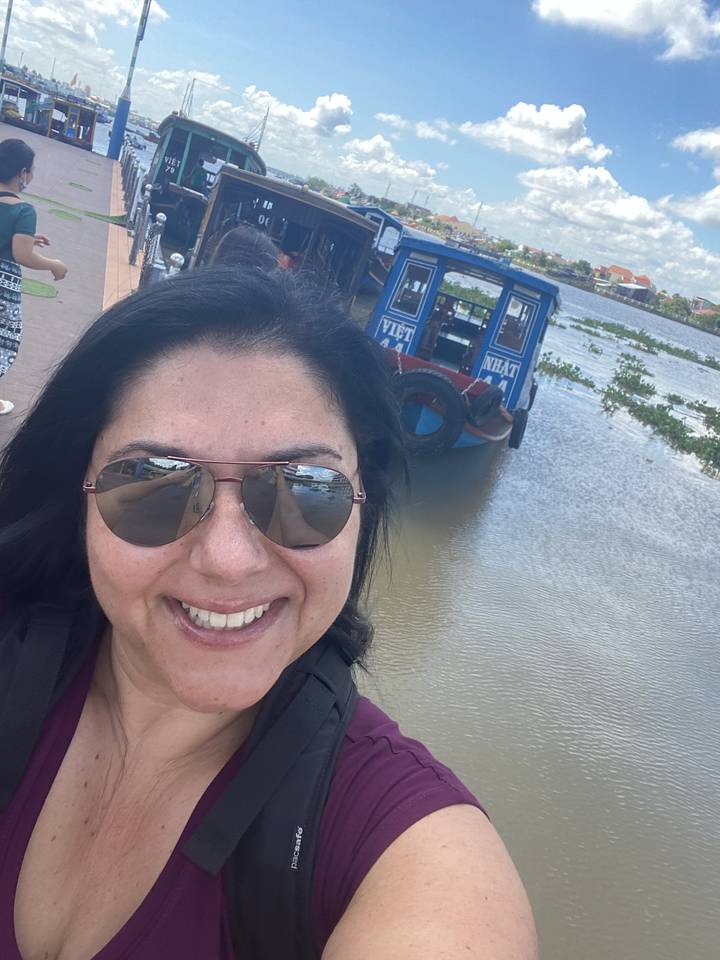 A person taking a selfie with a backdrop of boats on water.