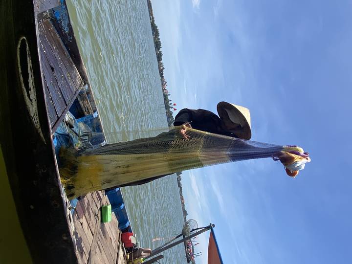 A person fishing with a traditional net in a river scene.