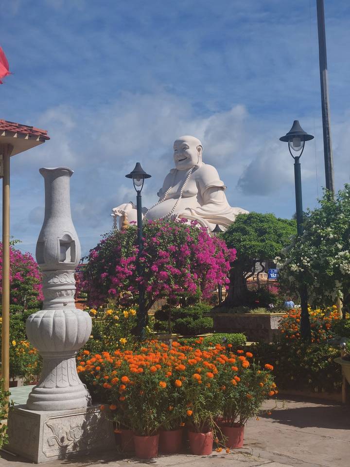 Large white Buddha statue surrounded by colorful flowers.