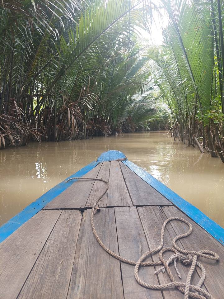 Boat navigating a narrow canal lined with dense vegetation.
