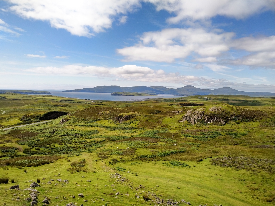 Expansive landscape with rolling green hills and view of a distant lake.