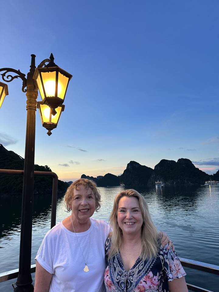 Deux femmes souriantes avec un magnifique paysage de falaises et d'eau derrière elles.