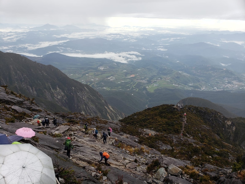 View from a high point showing hikers on a rocky path with a panoramic landscape.