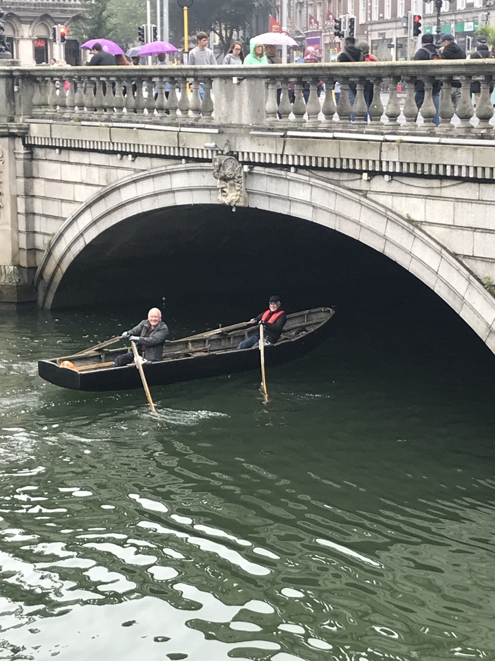 Two people rowing a small boat under a stone bridge.