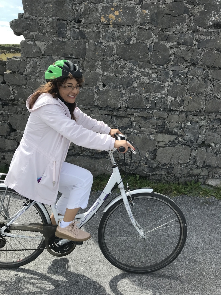 Woman in a raincoat riding a bicycle near a stone wall.