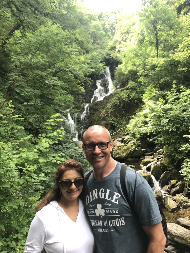 Couple posing in front of a lush waterfall surrounded by greenery.