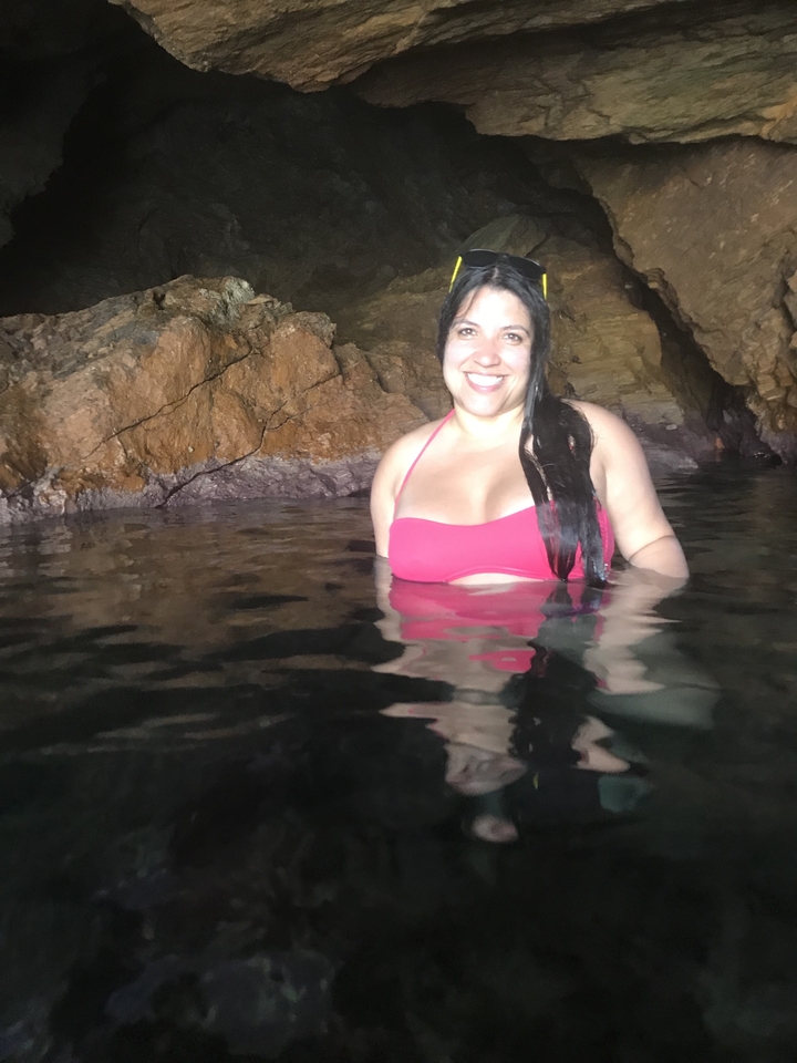 Femme en bikini souriante dans une grotte avec de l'eau.