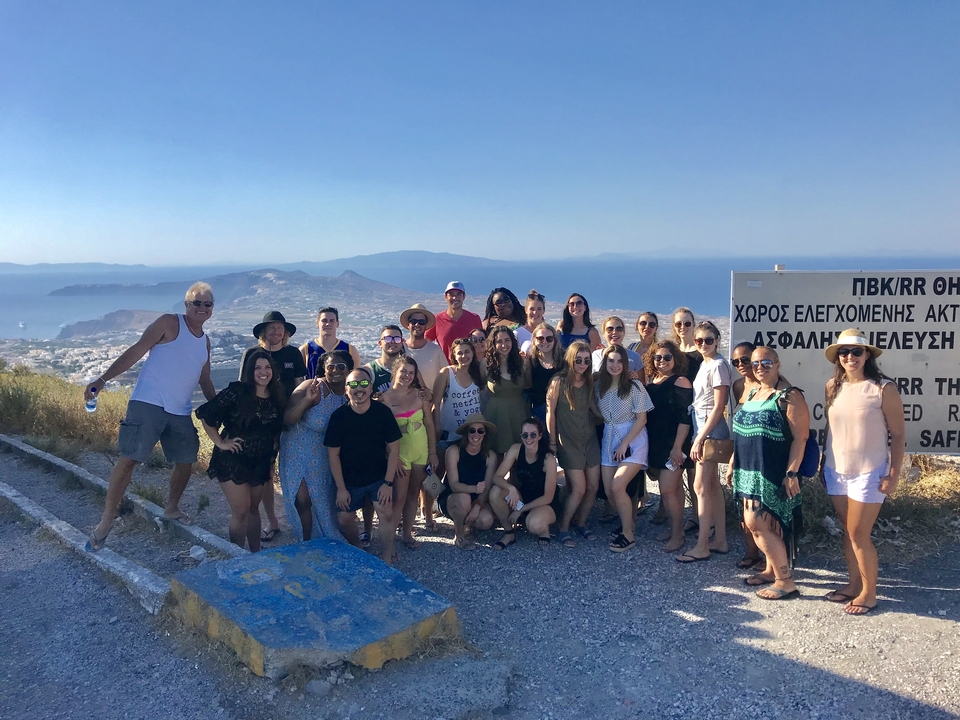 Grand groupe de personnes posant sur une colline avec la mer en arrière-plan.