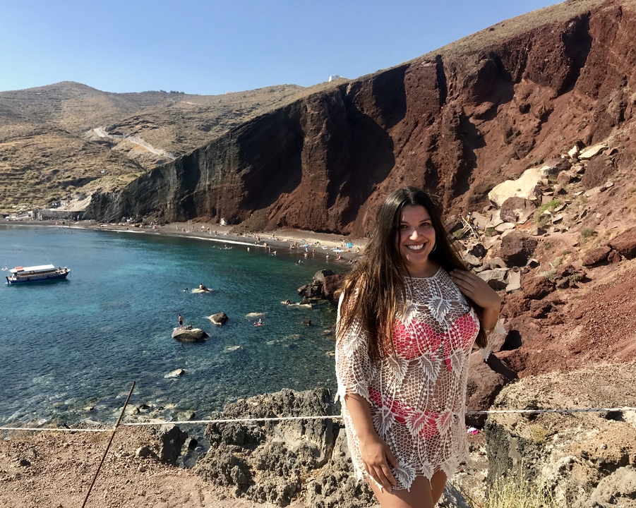 Femme souriante sur une plage rocheuse avec de l'eau bleue claire.