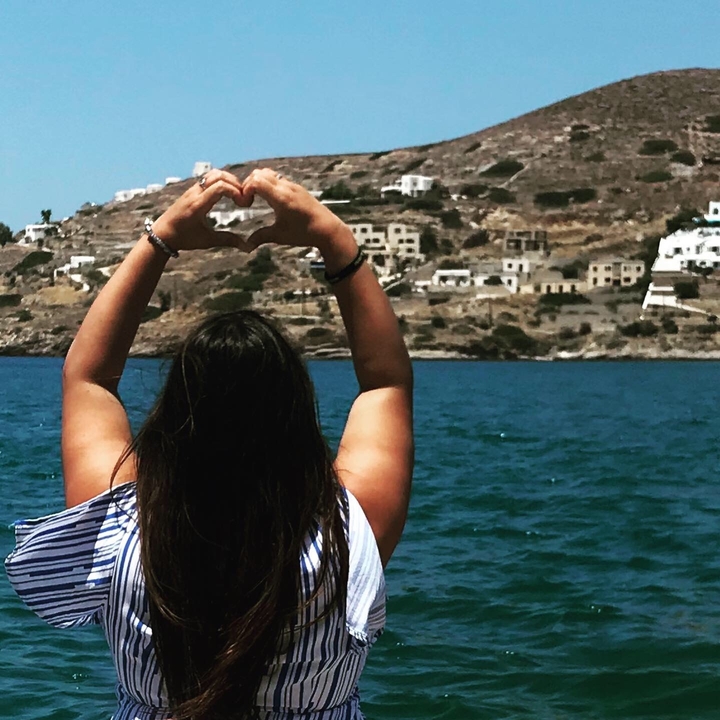 Une femme faisant une forme de cœur avec ses mains en regardant la mer.