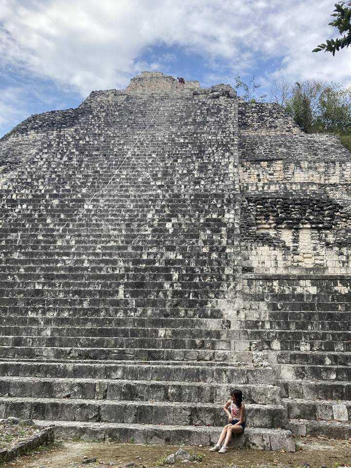Tourists sitting on the steps of a large stone structure.