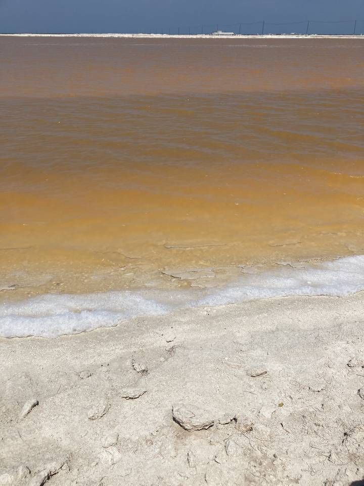 Sandy beach with orange water and nearby waves.