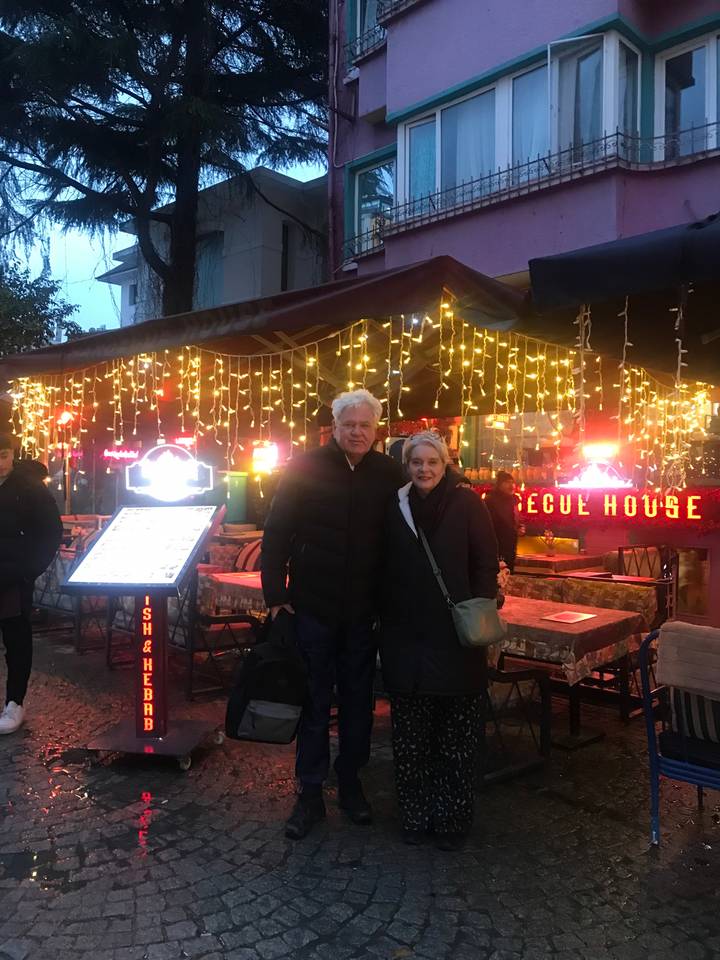 A couple standing outside a cafe with festive lighting at dusk.