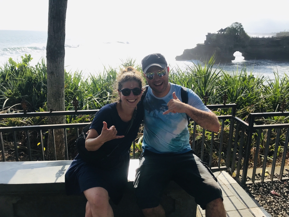 Two people posing with a scenic background of ocean and temple.