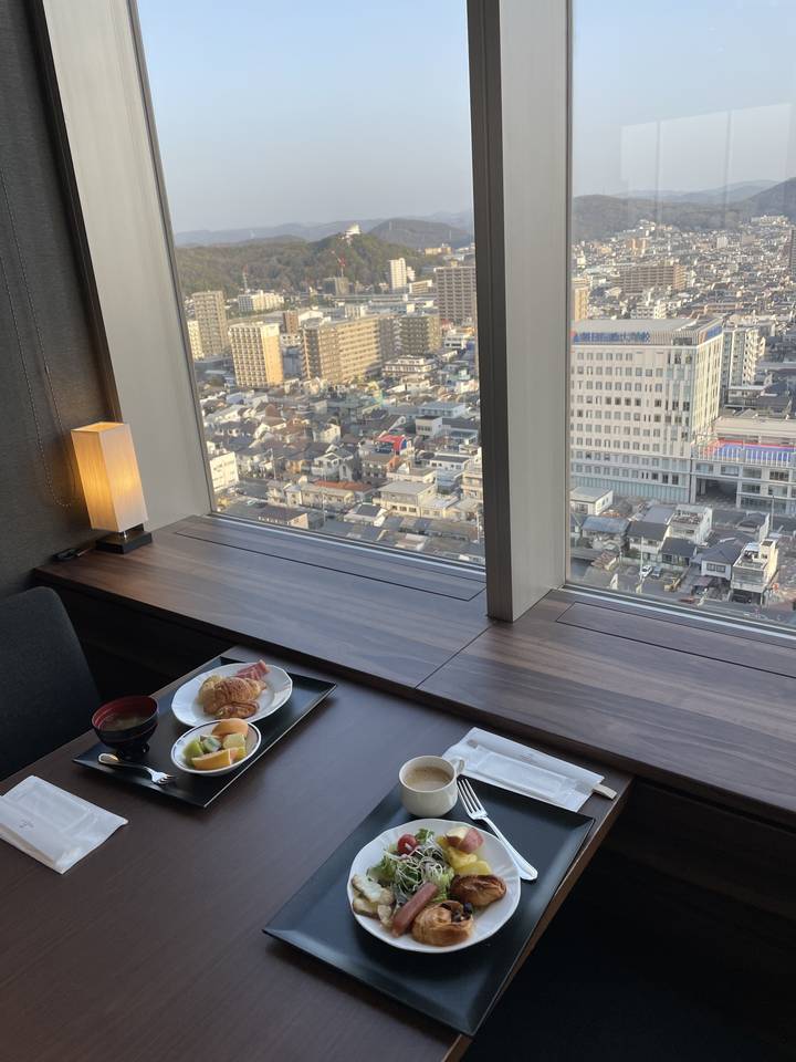 Table avec petit-déjeuner donnant sur une vue panoramique de la ville à travers une fenêtre.
