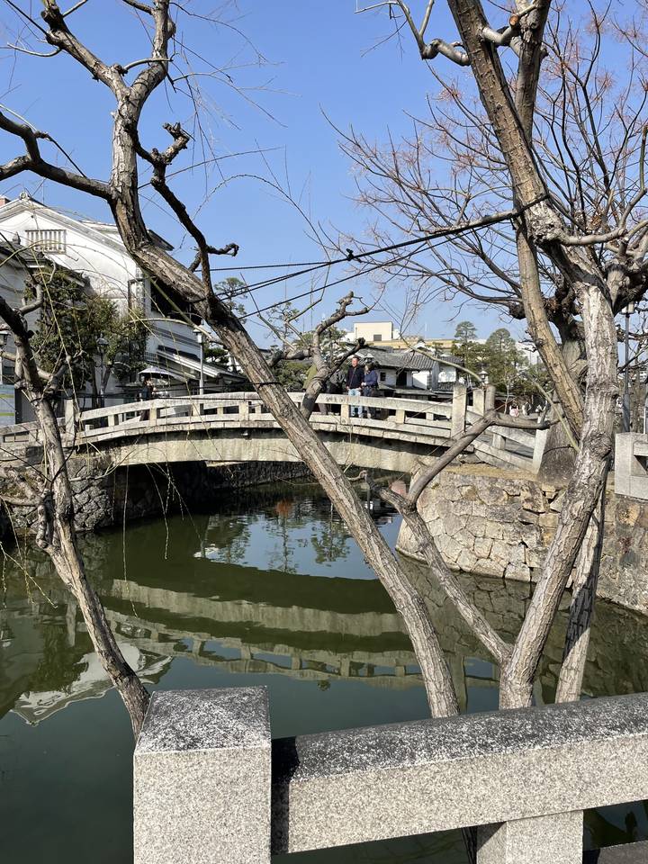 Reflets d'un pont et d'arbres dans une rivière sous un ciel bleu dégagé.