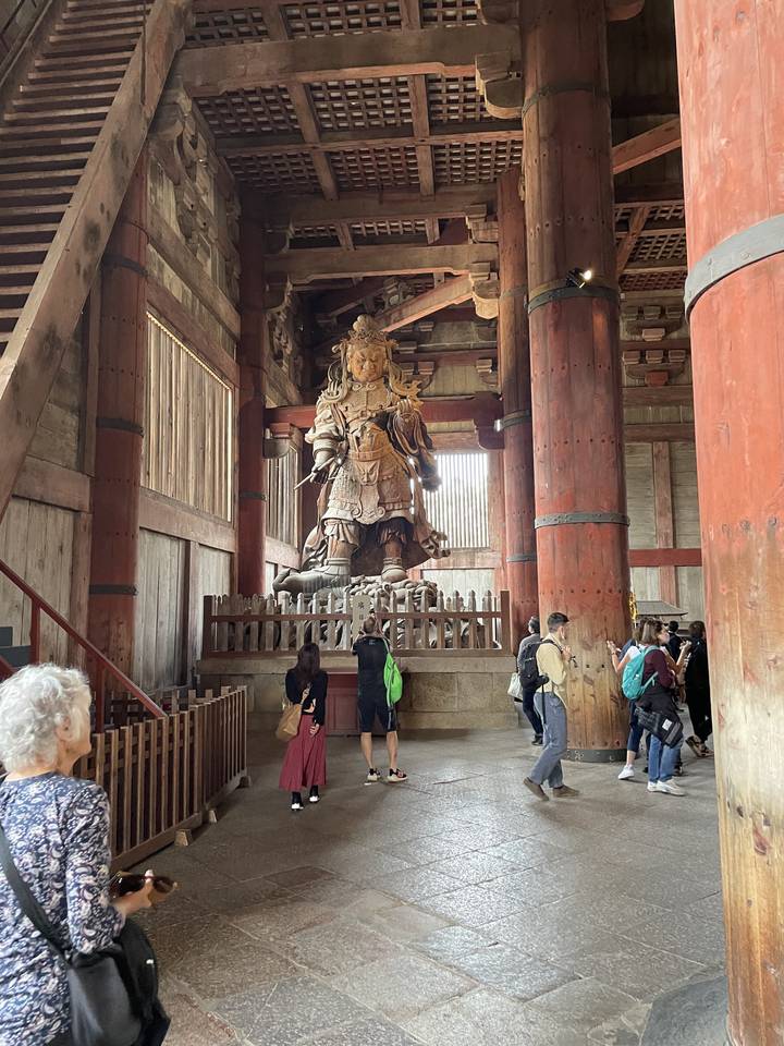 Intérieur d'un temple en bois avec une statue et des personnes qui observent.