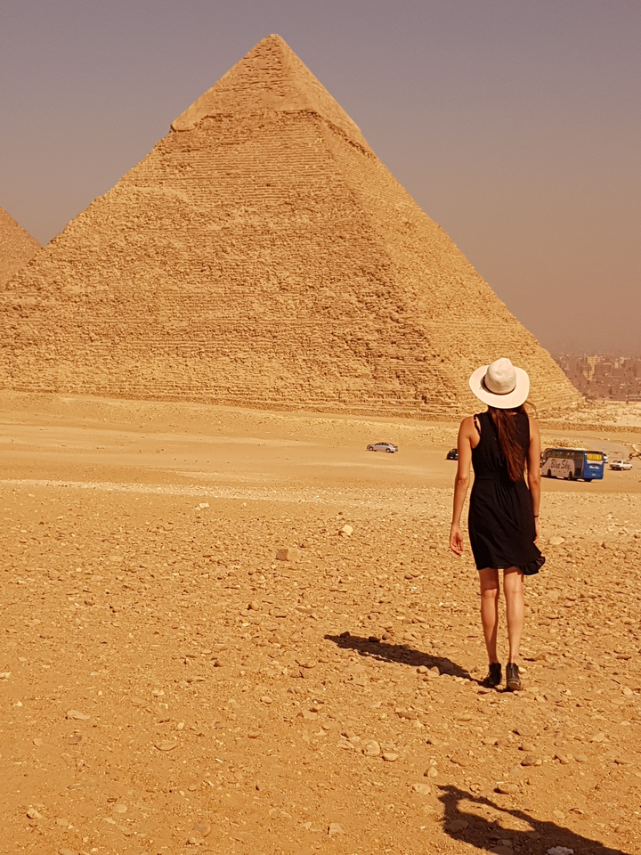 Woman walking towards a pyramid in the desert.