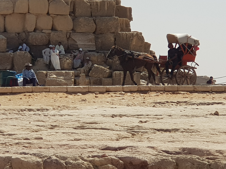 Horse-drawn carriage and people next to an ancient structure.