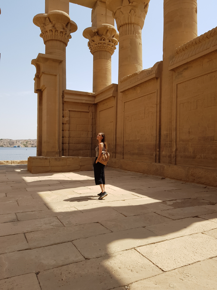 Woman standing next to ancient walls with carvings.