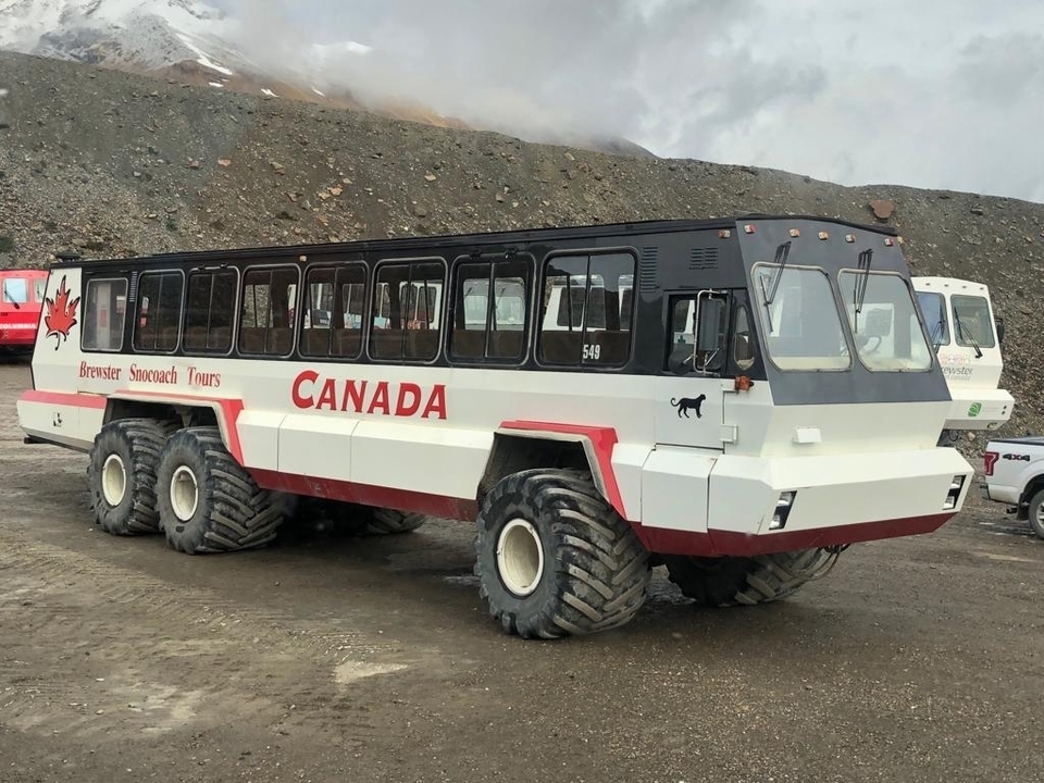 Snowcoach vehicle with large tires parked in a gravel area.