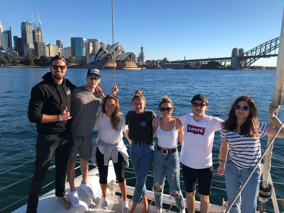 Des personnes debout sur un bateau avec l'Opéra de Sydney et le Harbour Bridge en arrière-plan.