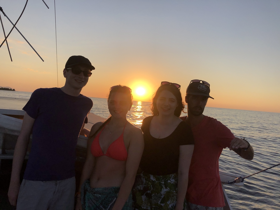 Groupe de quatre personnes sur un bateau au coucher du soleil.