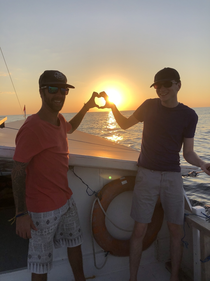 Deux personnes formant un cœur avec leurs bras au coucher du soleil sur un bateau.