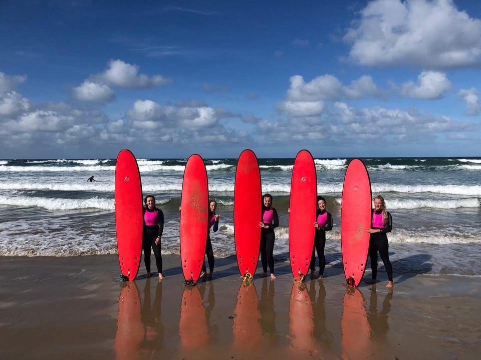 Group of people on a beach holding red surfboards in front of the ocean waves.
