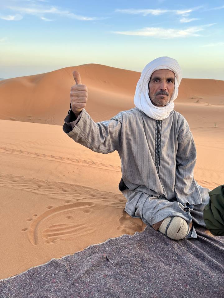 Man sitting in the desert with thumbs up.