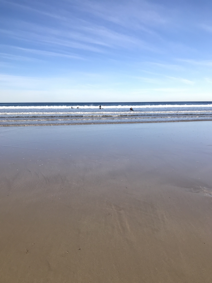Wide shot of a beach with waves and few people in the water.