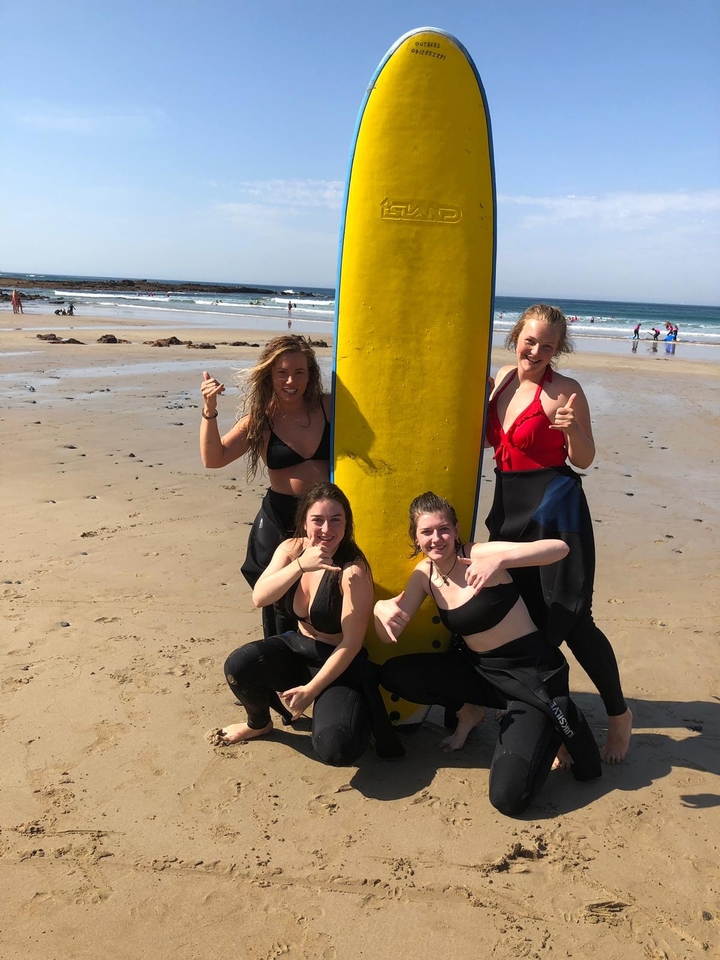 Four women posing with a surfboard on the beach.