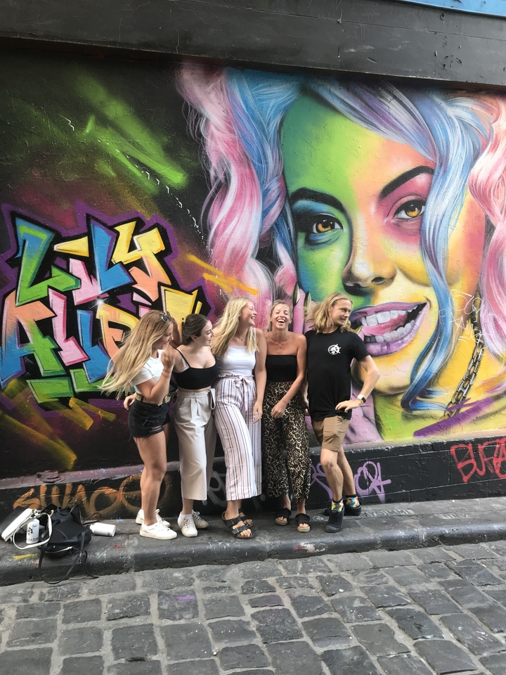 Group of people posing in front of colorful street graffiti.