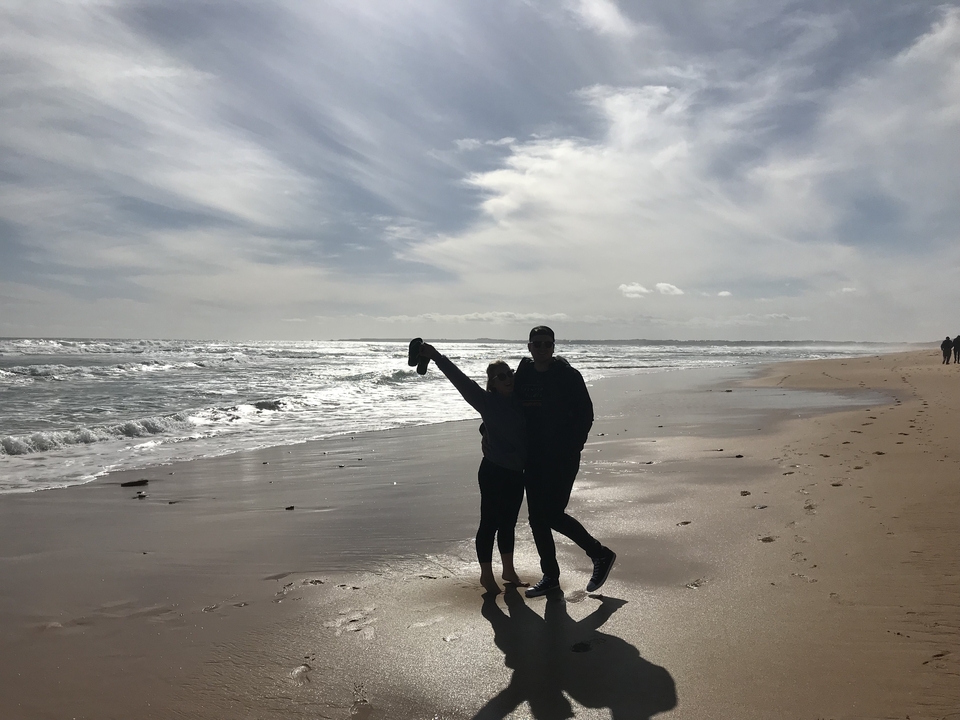 Couple posing on a beach, holding raised arms.