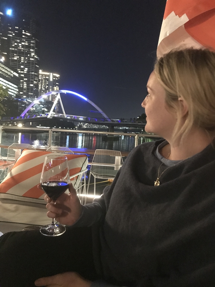 Person enjoying wine with a view of a lit-up bridge at night.