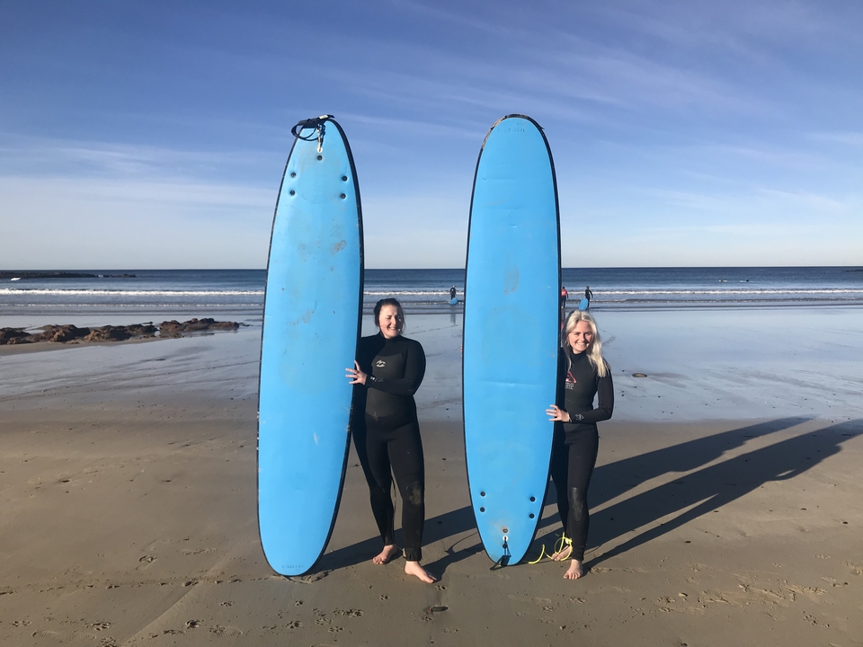 Two women holding surfboards on a beach.