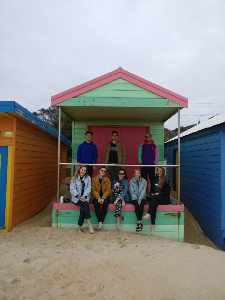 Group of people sitting in front of colorful beach huts.