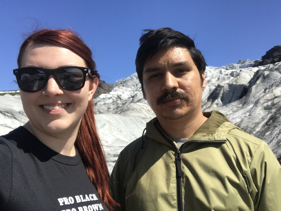 Two people posing in front of a glacier under clear skies.