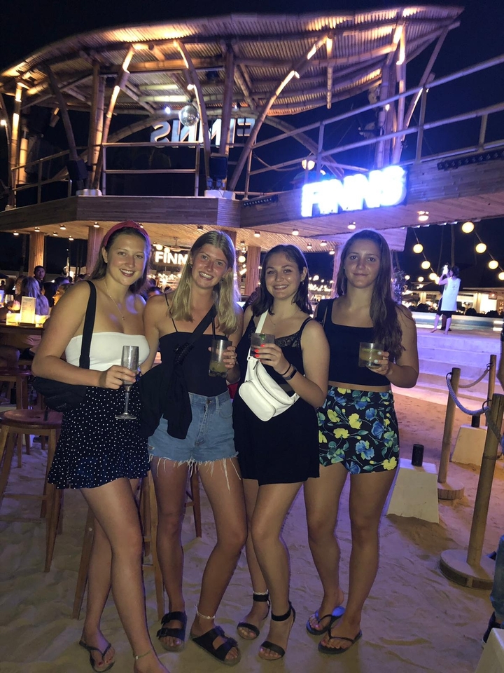 Quatre femmes tenant des boissons dans un lieu extérieur nocturne.